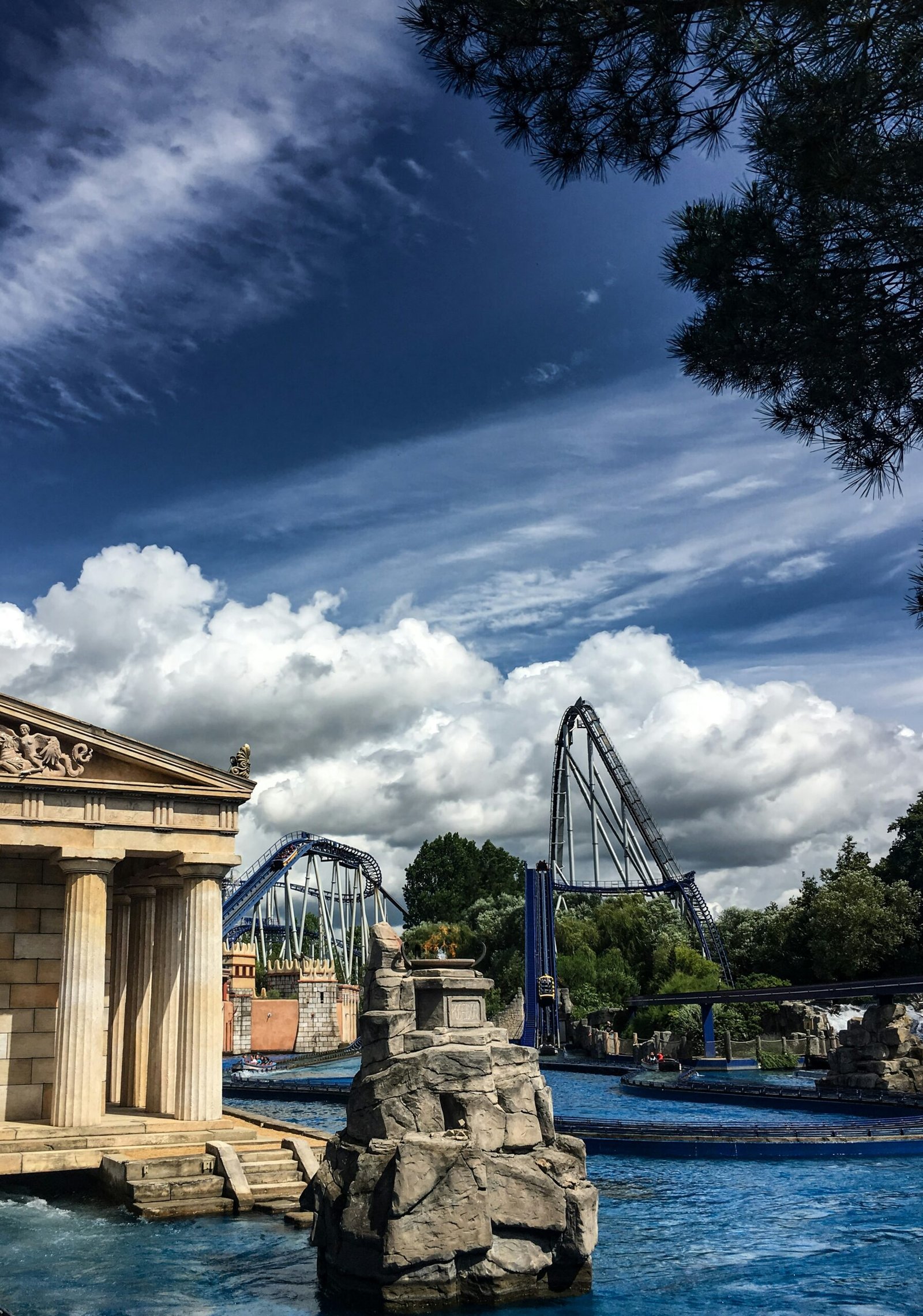 A water park with a fountain and a roller coaster in the background